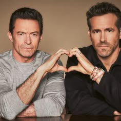 two men sitting at a table with their hands in the shape of a heart