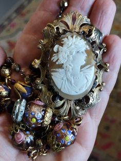 An amazing antique cameo I acquired unset. I've mounted it in a bezel with lace type scallops and then mounted it in a vintage brass Victorian style frame. To the back I added a vintage filigree finding with a vintage to antique pot metal button set with rhinestones. The cameo is a Bacchante goddess, a follower of Bacchus. She has beautifully detailed grape vines in her hair. To the bottom of the florid frame, I've added a large vintage Venetian wedding cake bead, vintage brass cap and large vintage brass and rhinestone rondelle. The cameo pendant hangs from the large brass link chain by two bezel set faceted pyrite gems. Accompanying pendants are Fire polished vintage Czech glass, vintage caps, vintage black refaceted Czech beads and two more large Venetian wedding cake beads. Finishes wi Black Cameo Necklace, Adjustable Antique Style Necklaces At Low Price, Vintage Filigree Baroque Jewelry, Ornate Antique Gold Cameo Necklace, Ornate Cameo Necklace In Antique Gold, Vintage Antique Gold Cameo Necklace, Bronze Cameo Jewelry For Vintage Collection, Vintage Cameo Necklace In Antique Gold, Antique Cameo Necklace For Vintage Events