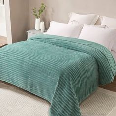 a bed with a green blanket and white pillows on top of it in a bedroom