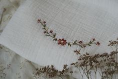 some flowers are laying on top of a white linen pillow case with embroidered edges and red stems