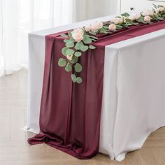 the table is set up with white and red flowers on it, along with greenery