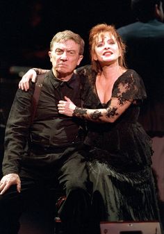 a man and woman sitting on top of each other in front of a stage curtain