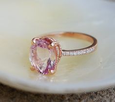 an oval shaped pink sapphire and diamond ring on a white plate with a shell in the background