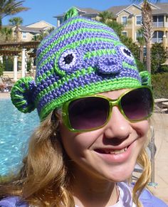 a woman wearing sunglasses and a crocheted hat by a swimming pool with palm trees in the background