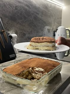 a person holding a plate with a cake on it and another serving one in the background