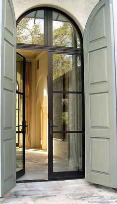 an open door leading to a patio with large windows and doors on both sides, in front of a white stucco building