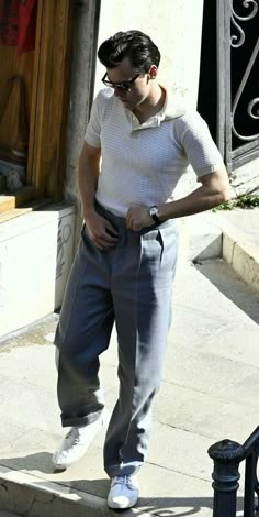 a man in white shirt and grey pants walking down the street with his hand on his hip