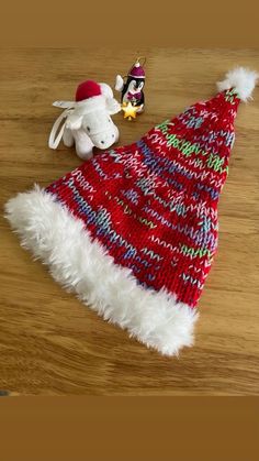 a red and white knitted christmas hat next to a small stuffed animal on a wooden table