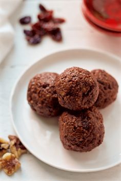 three chocolate cookies on a white plate next to nuts and dried cranberries in the background