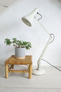 a white table lamp sitting next to a potted plant on a wicker stool