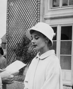 black and white photo of woman in hat holding papers with man standing next to her