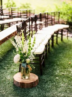 an arrangement of flowers and greenery sits on a wooden table in front of rows of chairs