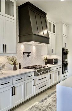 a large kitchen with white cabinets and black stove top range hood over an oven in the center