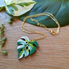 "Inspired by the Albo Borsigiana variegated monstera deliciosa, this unique heart-shaped leaf necklace will add a luxurious botanical flair to your wardrobe or bring a personal hand-made touch as a gift to a loved one. This original design is hand painted on cherry wood with a beautiful patchwork palette of white and green. The subtle heart shape of the leaf adds even more character to an already unique necklace. Lightweight and durable, this necklace is sure to capture the heart of any plant lover. Get ready for compliments! Option 1: Silver Finish This option comes with an 17.5\" silver-plated brass cable chain with a lobster clasp and 2\" extender chain.  Option 2: Gold Finish This option comes with a 17.5\" 16K gold-plated brass cable chain with a lobster clasp and 2\" extender chain. Handmade Heart Pendant Necklace With Nature-inspired Style, Handmade Heart Pendant Necklace, Nature-inspired, Handmade Tropical Green Jewelry, Handmade Green Leaf Necklace, Unique Leaf-shaped Necklace For Gifts, Unique Green Heart-shaped Necklace, Green Botanical Necklace For Gifts, Green Leaf-shaped Necklace For Gift, Green Botanical Necklace For Gift