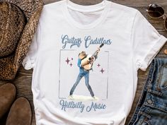 Guitars Cadillacs Hillbilly Music - Dwight Yoakam Vintage-Style Graphic Tee * Bella + Canvas soft fabric T-shirt * Unisex adult sizing * Direct-to-Garment printed item that will not peel like vinyl Care Instructions: *Wash item inside-out in cold water on gentle washing cycle *Dry on low heat or let air dry  *Do not iron directly onto the design *Please review the product photos for available styles, size, shirt colors and other details such as font color  ❤️ Thank you for supporting my small business! Cotton T-shirt With Letter Print For Country Festivals, Crew Neck T-shirt For Country Concerts And Festivals, Crew Neck T-shirt For Country Concerts, White Band Merch T-shirt For Country Concerts, Relaxed Fit Cotton T-shirt For Country Festivals, Relaxed Cotton T-shirt For Country Festivals, Band Merch Cotton T-shirt For Country Concerts, Cotton Band Merch T-shirt For Country Concerts, Music Tshirt