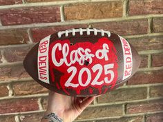 a hand holding a football with the words class of 205 painted on it in front of a brick wall