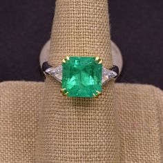 Absolutely stunning Colombian emerald mounted with 18k yellow gold  and platinum shank ! The 5.17CT emerald is from Colombia, beautiful rich green color and good clarity for its size. There are two sparkly trillion cut white diamonds adorning the center stone totaling 0.90 carat! This ring comes with one certification: Gemological Institute of America (GIA) Ring Size: 7 Total Weight: 8.2 grams Precious Metal: Platinum, 18k yellow gold Precious stones: -Emerald Center Stone: 5.17 carats, 10mmx10m Luxury Gia Certified Emerald Cut Gemstones, Luxury Gia Certified Emerald Gemstones, Luxury Emerald Gemstones With Prong Setting, Trillion Cut Emerald Ring For Formal Occasions, Luxury Trillion Cut Emerald Ring For Formal Occasions, Formal Gia Certified Emerald Gemstones, Luxury Gia-certified Trillion Cut Emerald Ring, Luxury Gia Certified Trillion Cut Emerald Ring, Elegant Green Gemstones Brilliant Cut