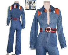 This deadstock 70s-era jumpsuit features a lovely vintage wash denim with western style serape patchwork and shoulder epaulettes on the bodice, matching belt with huge brass "militaires equipment" buckle, interesting 60s/70s style hip pockets, and flared bell bottom pant legs. This piece has never been worn and still has original price tag attached. Jumpsuit is 100% cotton, unlined and zips up the front. Best fits size xxs or xs (please check measurements below). Accessories not included. Payment plans available. Approximate Flat Measurements:  Multiply times 2 for bust, waist, and hip measurements. For best fit, compare with a similar style of clothing which you already own.  Total Length: 56.5" Bodice Length: 15.5" Pant Length: 41" Inseam: 31" Rise: 12" Shoulder to Shoulder: 14" Sleeve L Vintage Jumpsuits And Rompers For Fall, Fitted Blue Denim Retro Jumpsuit, Retro Cotton Fitted Jumpsuits And Rompers, Retro Fitted Long Sleeve Jumpsuits And Rompers, Vintage Fitted Long Sleeve Denim Jumpsuit, Fitted Vintage Denim Jumpsuit With Long Sleeves, Blue Fitted Vintage Denim Jumpsuit, Vintage Fitted Long Sleeve Jumpsuits And Rompers, Vintage Cotton Fitted Denim Jumpsuit