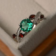 a ring with an oval cut green stone surrounded by garnets in a box