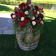 a wooden barrel filled with lots of red and white flowers on top of grass next to a lake