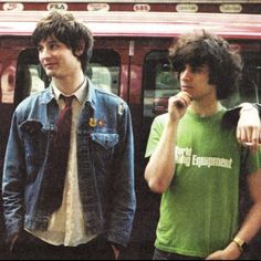 two young men standing next to each other in front of a train