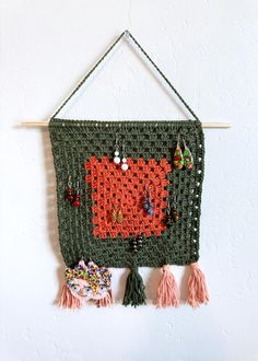 a crocheted wall hanging with tassels and earrings on it, attached to a white wall