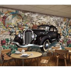 an old car is parked in front of a graffiti covered wall with tables and chairs