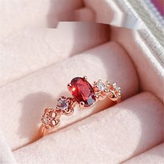 an engagement ring with a large red stone surrounded by small white diamonds in a box