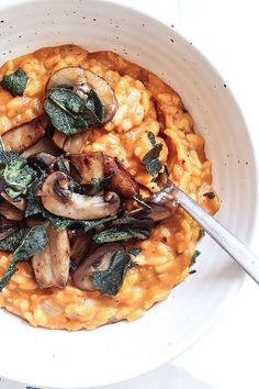 a white bowl filled with pasta and mushrooms on top of a table next to a fork