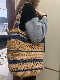 a woman carrying a crocheted bag in front of a mirror with her hand on her shoulder