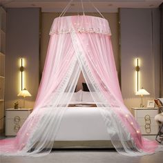 a pink canopy bed in a bedroom with white furniture and lights on the wall behind it