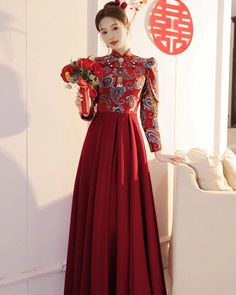 a woman in a long red dress standing next to a white vase with flowers on it