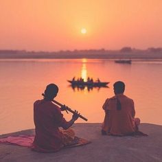 two people sitting on the edge of a body of water