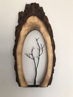 an oval wooden frame with a tree branch in the center and a white wall behind it