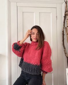 a woman in a red and black sweater leaning against a door with her hand on her head