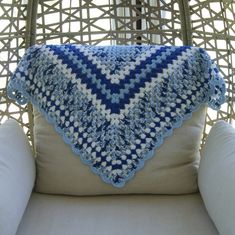 a blue and white crocheted blanket sitting on top of a chair next to a pillow