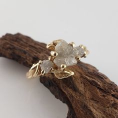 a gold ring with two white stones on it sitting on top of a piece of wood