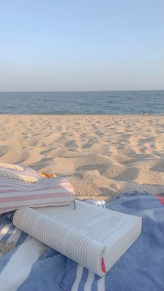 an open book sitting on top of a blue blanket next to the ocean and beach