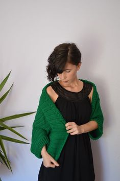 a woman standing in front of a plant wearing a green knitted sweater and black dress