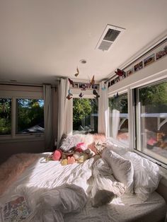 an unmade bed in front of two windows with birds hanging from the window sill