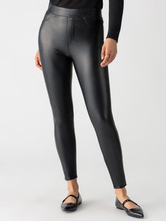 A person is shown from the shoulders down, wearing Sanctuary Clothing's Runway Legging Slick Black and a black long-sleeved top. They are also wearing black flat shoes and a simple gold ring. The background is plain white. Stretch Solid Color Polyurethane Leather Pants, Sleek Stretch Black Leather Pants, Sleek Black Stretch Leather Pants, Sleek Solid Color Faux Leather Leggings, High Stretch Sleek Solid Leggings, Black High Stretch Full Length Leather Pants, Sleek High Stretch Solid Color Leggings, Stretch Full-length Black Leather Pants, Sleek Solid High Stretch Leggings