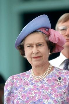 the queen of england is wearing a purple dress and blue hat with pink flowers on it