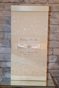 the wedding card is on display in front of a brick wall with a ribbon and bow