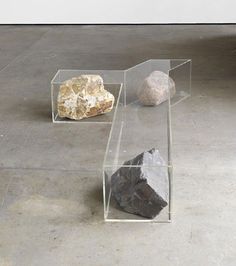 three rocks sitting on top of a cement floor next to each other in a glass case