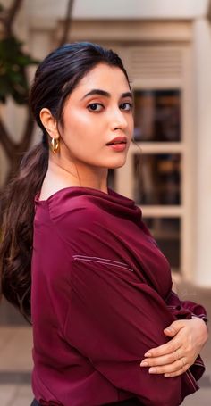 a woman with long hair wearing a maroon shirt and black pants is looking off to the side