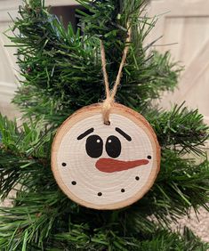 a wooden ornament hanging from a tree with a snowman face painted on it