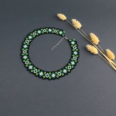 a green and white beaded necklace next to some dry flowers on a gray surface