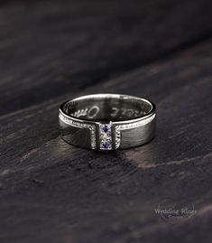 a white gold ring with blue and white diamonds on the side, sitting on a wooden surface