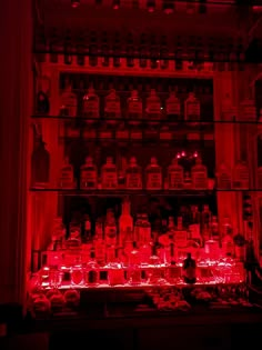 a shelf filled with bottles and glasses in a room full of red light from the ceiling