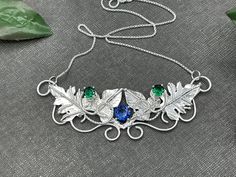 I've handmade this beautiful Woodland Leaves Elvish-inspired necklace keepsake, perfect for a Woodland wedding theme, or any event you desire! I've designed this in sterling silver with 3 gemstones. The top two are 4mm round faceted (emeralds shown in the images) and a center 6mm faceted gemstone of your choice. The pictures show 4 with a Rainbow Topaz for a lovely matching combination. Please contact me if you want specific gemstone choices not shown. I can accommodate most! Upon your order, pl Artisan Birthstone Necklace For Gifts, Custom Silver Necklaces For Anniversary, Sterling Silver Nature-inspired Necklace For Anniversary, Nature-inspired Sterling Silver Necklace For Anniversary, Artisan Wedding Necklaces With Unique Variations, Unique Birthstone Necklace For Anniversary, Whimsical Silver Round Pendant Necklace, Nature-inspired Pendant Jewelry For Crafting, Handmade Silver Whimsical Jewelry